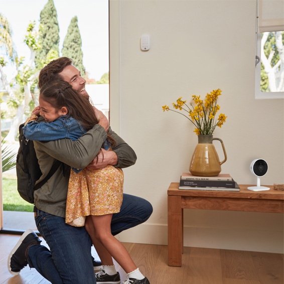 The Yale Smart Indoor Camera on a side table next to a front door, as a father hugs his daughter